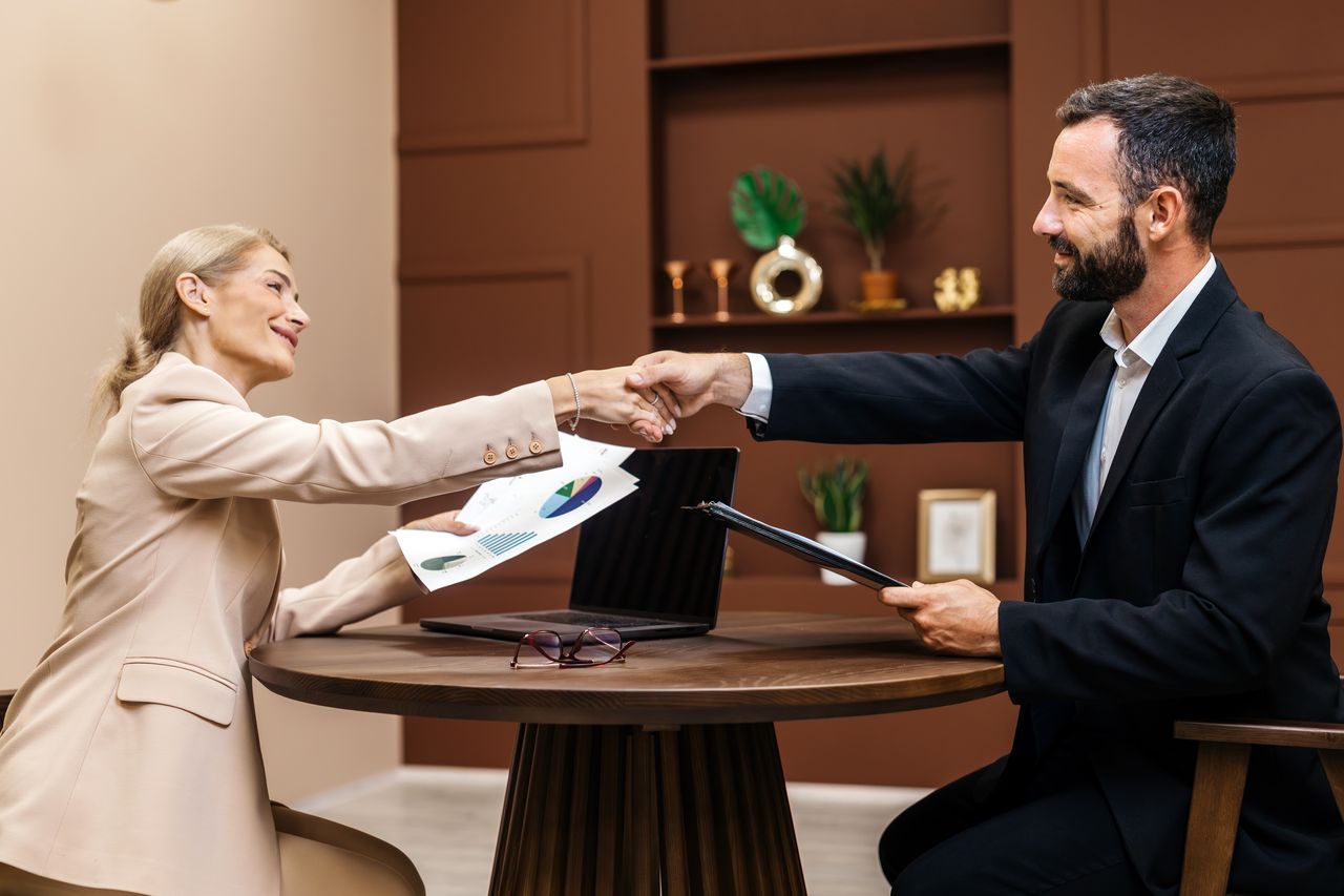 Vente grand compte réussie : équipe commerciale en RDV client, poignée de main, documents et graphiques stratégiques.